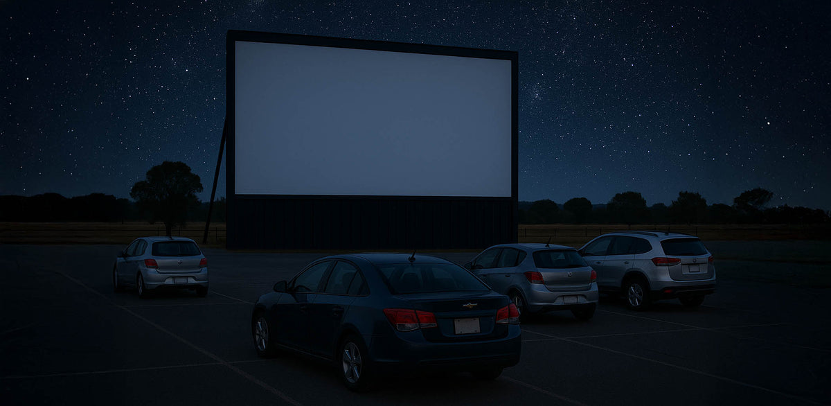 Drive-in theater with cars parked under a large screen at night.