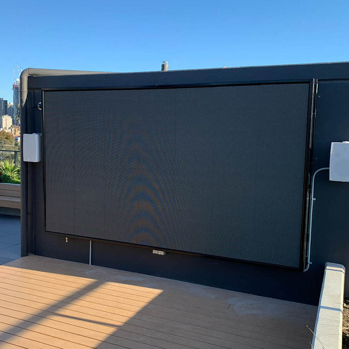 Large outdoor LED screen mounted on a rooftop with speakers mounted to the wall with city skyline in the background