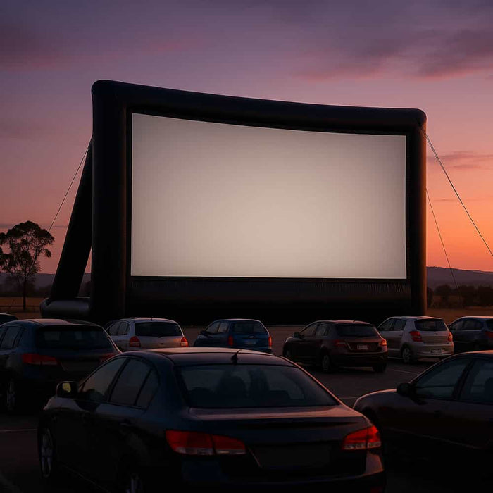 Sunset drive-in scene with cars parked before a huge inflatable outdoor movie screen.